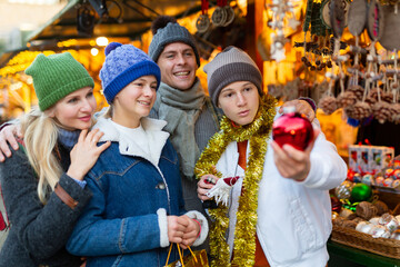 Friendly family with teenage children who came to the Christmas fair in the open air, chooses Christmas souvenirs and toys