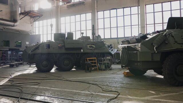 A hangar with military armored vehicles that stand in a row. The camera shoots military equipment