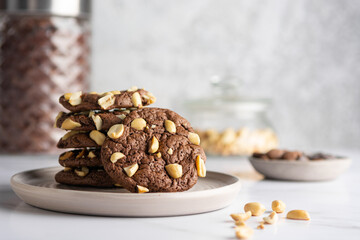 Stack of chocolate brownie cookies with peanuts on a ceramic plate with nuts, chocolate drops and...