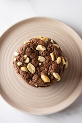 Chocolate brownie cookies with roasted peanuts, top view. On a ceramic plate on a white marble background
