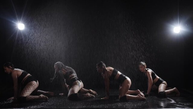 Four women in sexy clothes and mesh tights dancing in a row under the rain