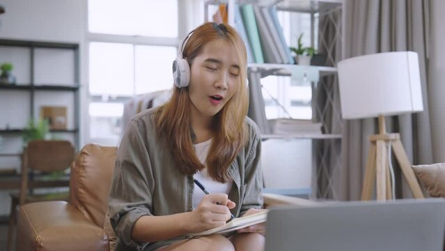 Young asian female wear earphone write down the meeting information in a notebook.