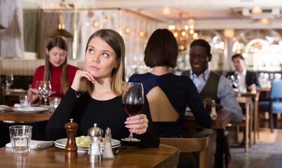 Portrait of thoughtful attractive girl with wine glass dining all alone in cozy restaurant .