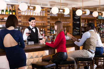 Adult people are relaxing near bar counter and drinking alcohol in restaurant