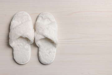 Pair of soft slippers on white wooden floor, top view. Space for text