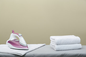 Modern iron and clean towels on board against beige background. Space for text