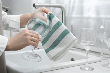 Woman wiping glass with towel near sink in kitchen, closeup