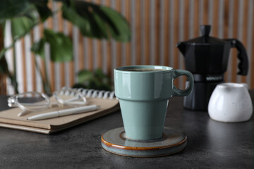 Mug of hot drink with stylish cup coaster on grey table