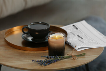 Beautiful candle, lavender, newspaper and cup of coffee on round wooden table indoors