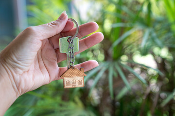Fototapeta premium Hand holding house key with palm tree nature background. Home ownership concept.