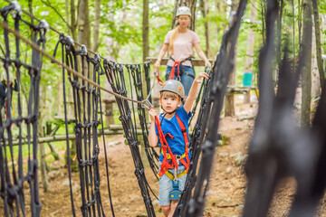 Mother and son climbing in extreme road trolley zipline in forest on carabiner safety link on tree to tree top rope adventure park. Family weekend children kids activities concept Portrait of a