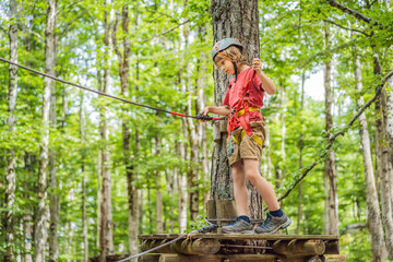 Naklejka na ściany i meble Happy child in a helmet, healthy teenager school boy enjoying activity in a climbing adventure park on a summer day