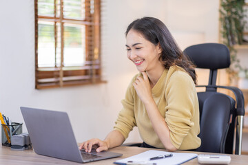 Smiling indian woman using laptop at home, Happy Young asian  businesswoman send email and working at home. Asian freelancer typing on computer with paperworks and documents on table.