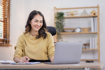 Smiling indian woman using laptop at home, Happy Young asian  businesswoman send email and working at home. Asian freelancer typing on computer with paperworks and documents on table.