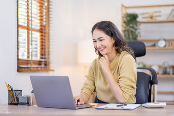 Obraz premium Smiling indian woman using laptop at home, Happy Young asian businesswoman send email and working at home. Asian freelancer typing on computer with paperworks and documents on table.