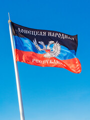 Flag of Donetsk People's Republic (DPR or DNR) with coat of arms in the center. Vertical against blue sky background. War in eastern Ukraine (Donbas) concept.
