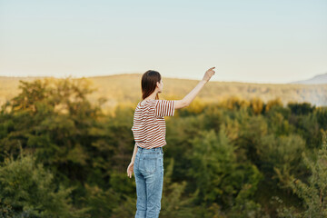 A young woman stands with her back to the camera in a T-shirt and jeans in nature and admires a beautiful view of the mountains