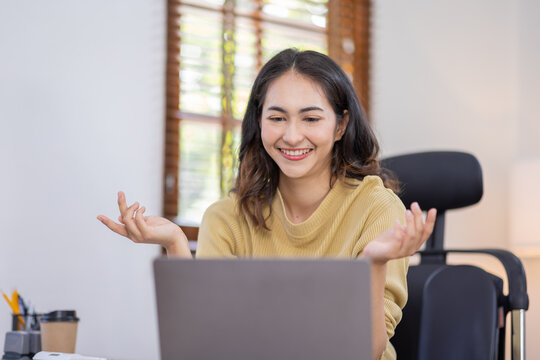 Image of young indian pleased happy cheerful cute beautiful business Asian woman sit indoors in home office using laptop computer talking in a video conference on line 