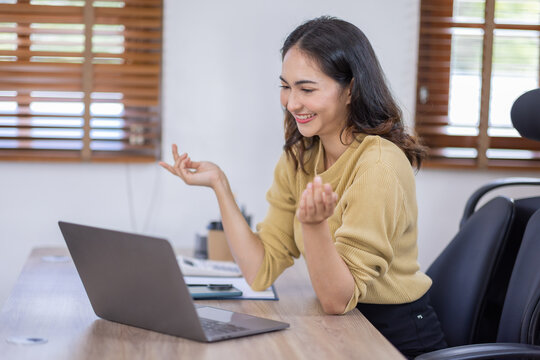 Image of young indian pleased happy cheerful cute beautiful business Asian woman sit indoors in home office using laptop computer talking in a video conference on line 