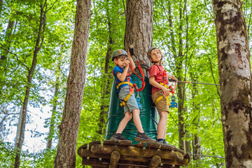 Two boys in a helmet, healthy teenager school boy enjoying activity in a climbing adventure park on a summer day
