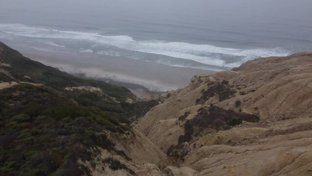 Aerial drone view of yellow sandstone cliffs gliding towards pacific coastline  during a foggy morning, Torrey Pines State Natural Reserve, San Diego, California
