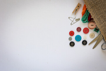 Sewing supplies spilling from hemp fabric bag. Scissors, various color treads and buttons on white background.