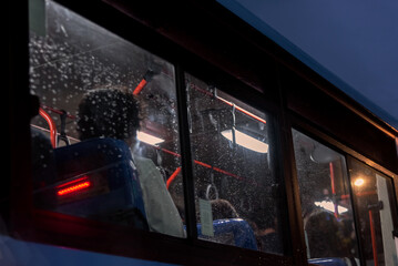 People heading home after a tiring day seen through a rainy bus window