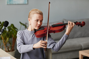 Portrait of blonde young woman playing violin at home or practicing in music studio, copy space