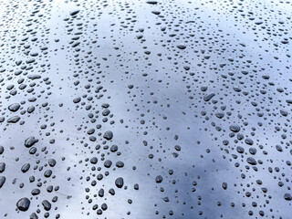 Raindrops on the hood of a shiny blue car reflecting clouds.