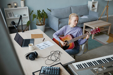 High angle portrait of blonde young woman playing guitar at home and composing music, copy space