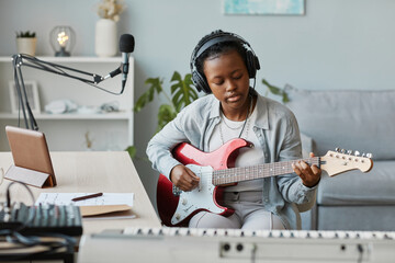 Portrait of young black woman playing electric guitar and recording songs in home studio, copy space