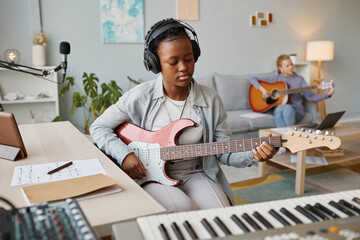 Portrait of young black woman playing electric guitar in studio and composing music, copy space