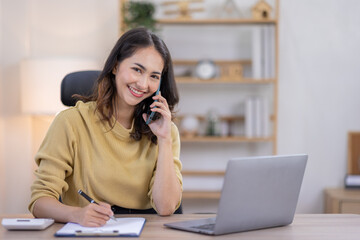 Freelance Smiling indian female young asian business woman using computer laptop and Talking Phone Working on Laptop In home Office.