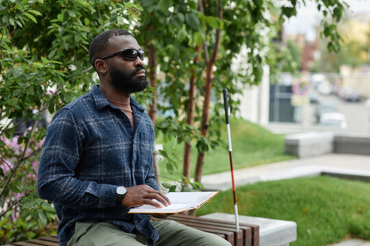 Portrait Of Blind Man Wearing Sunglasses And Reading Book In Braille Outdoors, Copy Space