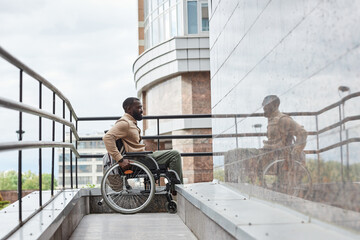 Full length side view of man with disability pushing wheelchair wheel while going down ramp in...