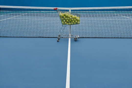 Horizontal no people shot of cart full of yellow tennis balls and net in blue colored court, professional sport concept, copy space