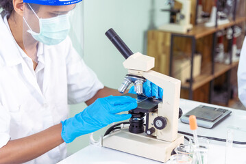 Naklejka premium Indian Scientist man look into Microscope research in science laboratory. Asian biochemistry scientist using microscope in laboratory chemistry labs. Covid-19 medical research scientific experiment