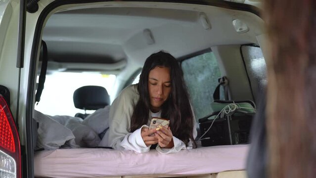 van life lifestyle , young mixed race woman living in rv camper resting on his bed playing with smartphone posting photo on social media