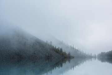 Tranquil meditative misty scenery of glacial lake with pointy fir tops reflection at early morning....
