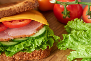 Part of the sandwich close-up on a wooden board with lettuce and tomato leaves. The concept is a photo of a delicious meal. 