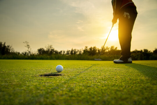 golfer putting a golf ball into a last hole on the green, golf course on summer sunset evening time with copy space