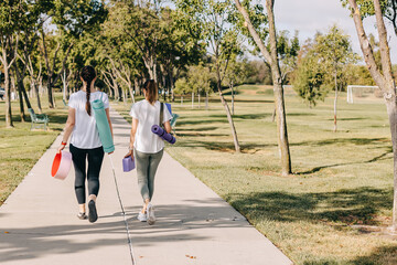 Two young women walking in the morning park, going to do yoga outdoors