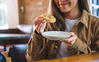 Closeup image of a young woman holding and eating at a piece of cookie
