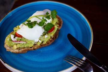 Healthy avocado toasts for breakfast or lunch with rye bread, sliced avocado and poached eggs