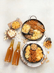 Assortment of beer and salty snacks on light background.