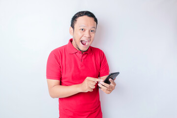 Surprised Asian man wearing red t-shirt pointing at his smartphone, isolated by white background