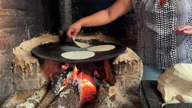 Mujer mexicana torteando maza de ma&iacute;z en un metate y una estufa de le&ntilde;a para hacer tortillas