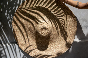 woman holding big straw hat with palm shadow on it.
