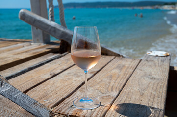 Glasses of cold rose wine from Provence served outdoor on wooden yacht pier with view on blue water and white sandy beach Plage de Pampelonne near Saint-Tropez, France