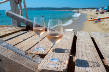 Glasses of cold rose wine from Provence served outdoor on wooden yacht pier with view on blue water and white sandy beach Plage de Pampelonne near Saint-Tropez, France